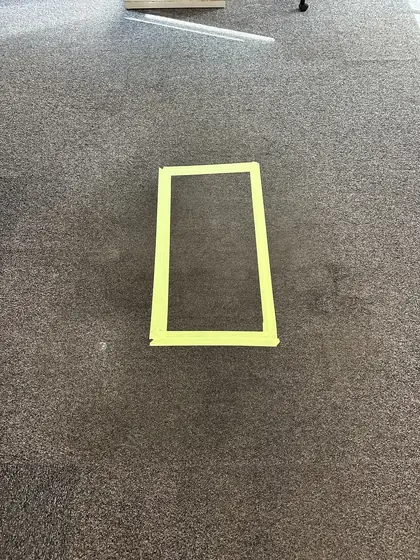 A rectangle taped off on a heavily soiled commercial carpet before cleaning